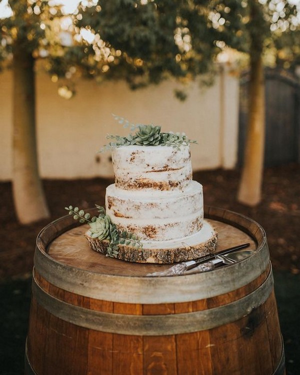 semi naked wedding cakes topped with greens on a wine barrel