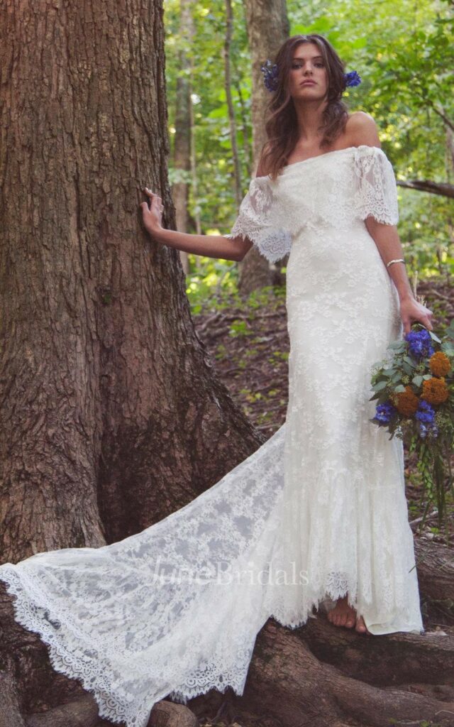 This Mexican wedding dress boasts a bohemian-inspired design with off-shoulder sleeves, intricate scalloped lace details, and a flowing train for a stunning and unique look.