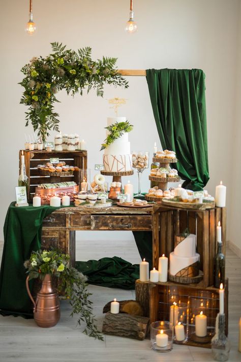 an elegant boho dessert bar with rustic crates, dozens of candles, a frame with foliage, dark green curtains and bulbs