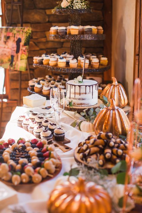 An autumn-themed rustic dessert table with wood cutting boards, pumpkins, leaves, and tree slices for serving food