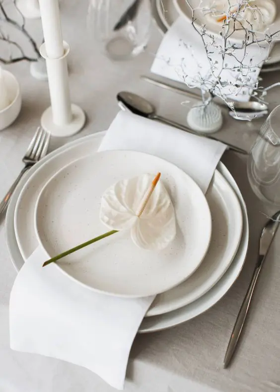 a lovely neutral wedding tablescape with all neutral everythingw ith white candles in white candlesticks elegant cutlery