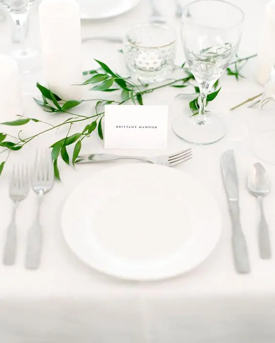 a minimalist and airy tablescape in white with candles and a touch of fresh greenery is a very fresh and cool idea