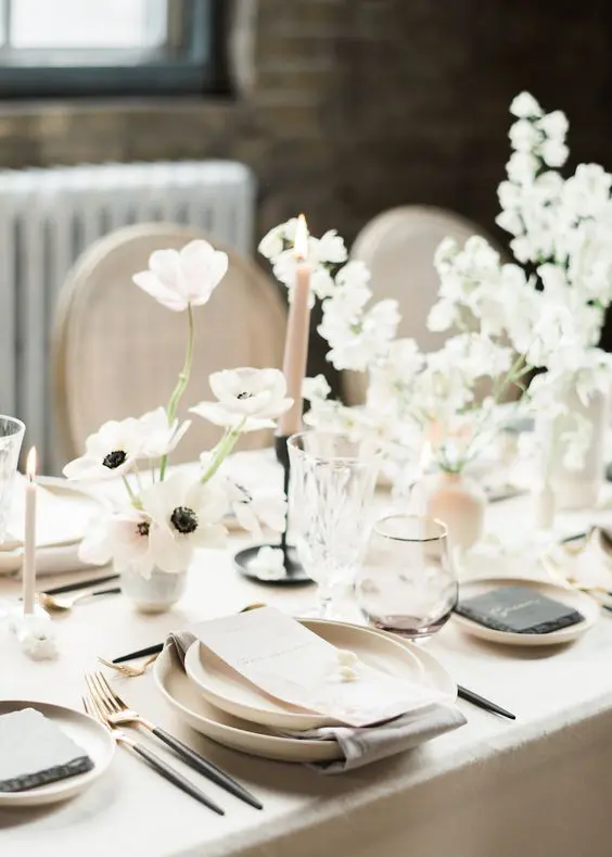 a minimalist and ethereal neutral wedding tablescape with neutral linens plates blush candles and white and blush floral arrangements