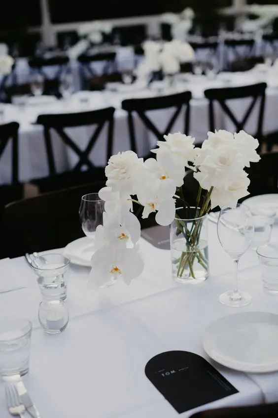 a refined minimalist wedding tablescape with crispy white linens white roses and rochids white plates and black menus