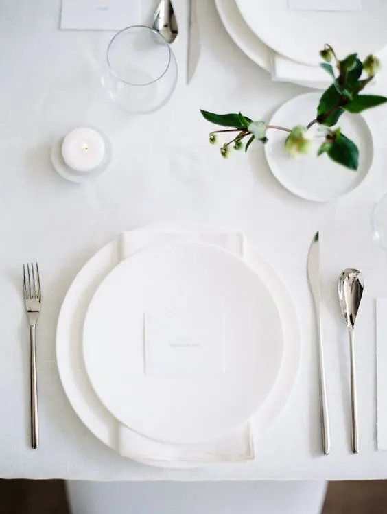 a white all minimalist wedding tablescape with all white everything some greenery to refresh the look and candles