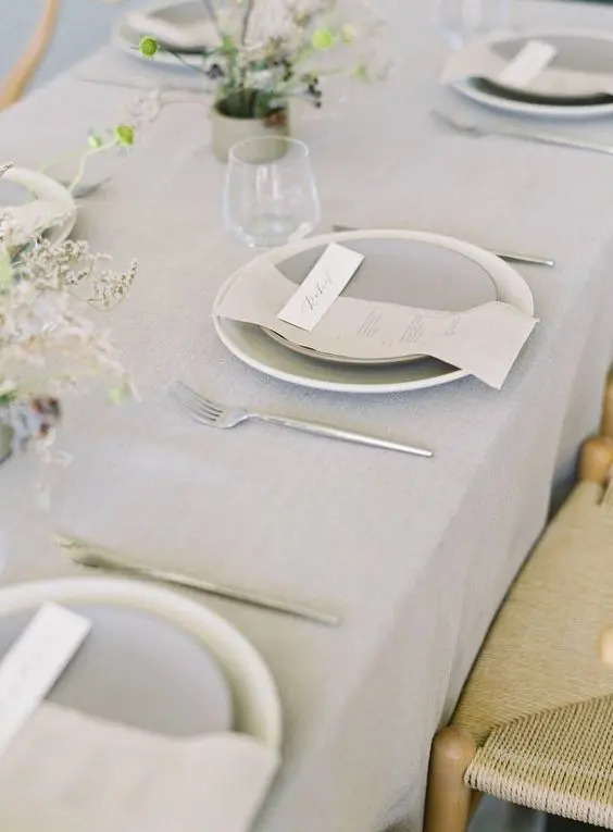 an airy minimalist wedding tablescape with a grey tablecloth plates and napkins dried blooms and candles is a stylish idea