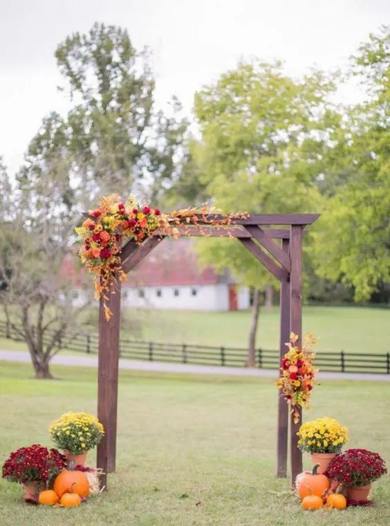 a bold rustic wedding arch of dark stained wooden slabs bright blooms and greenery and pumpkins and flowers around