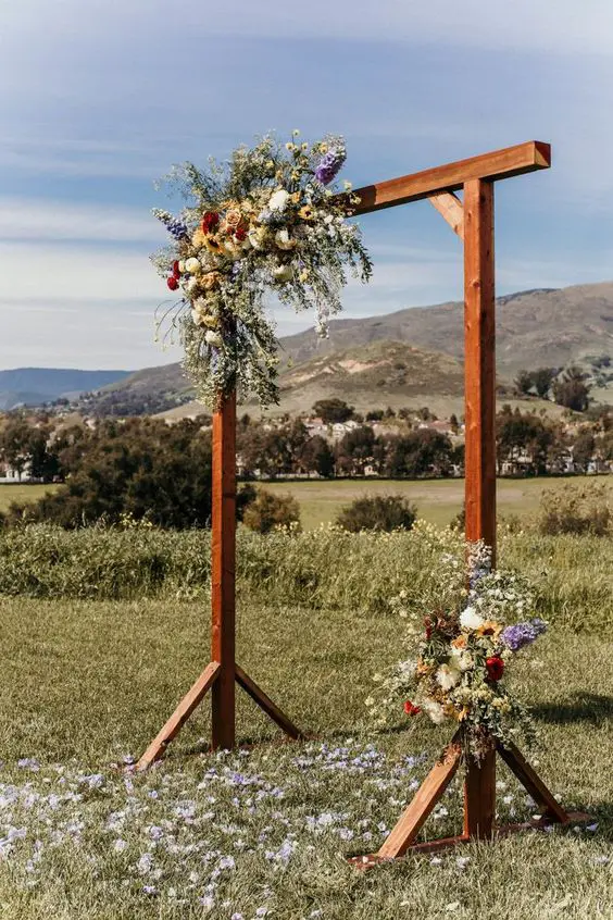 a bright rustic wedding arch of wooden slabs greenery and colorful blooms is a lovely idea for both an indoor and outdoor wedding