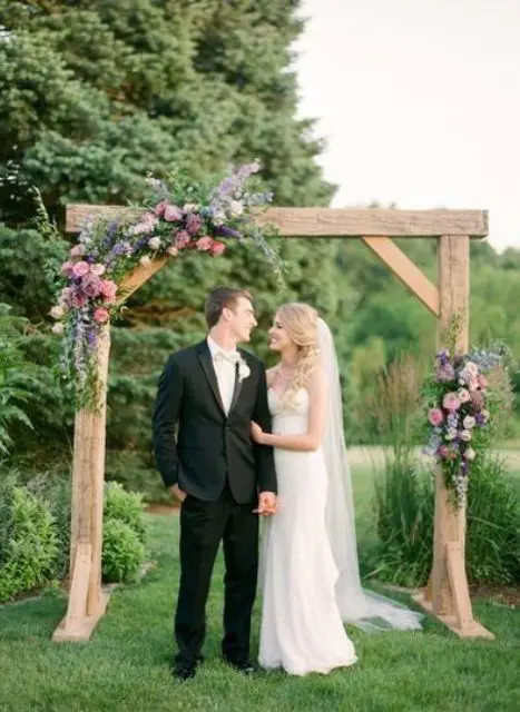 a cute summer rustic wedding arch of wood greenery mauve and pink blooms is a cool idea for a rustic summer wedding