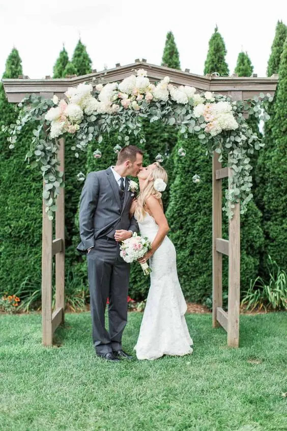 a rustic wedding altar covered with eucalyptus white hydrangeas and blush blooms is a stylish idea for a summer wedding