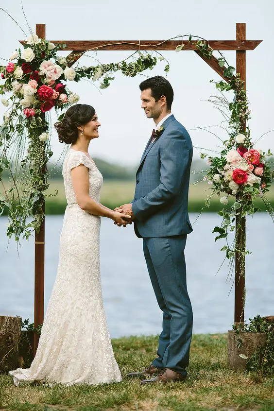 a rustic wedding arch of wood with greenery white pink and burgundy blooms and with a lovely lake view