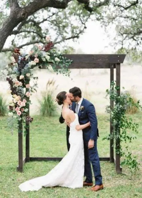 a stylish rustic wedding arch of dark wood white pink and burgundy blooms and greenery is a cool solution for a fall wedding