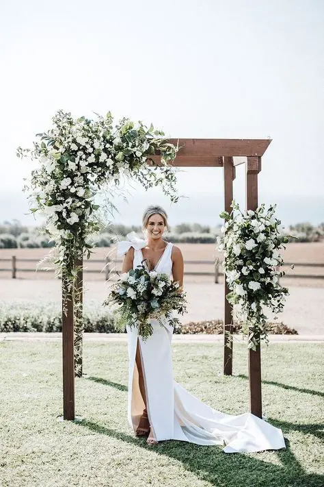 a stylish rustic wedding arch of wooden slabs greenery and white blooms is a timeless idea for a rustic wedding