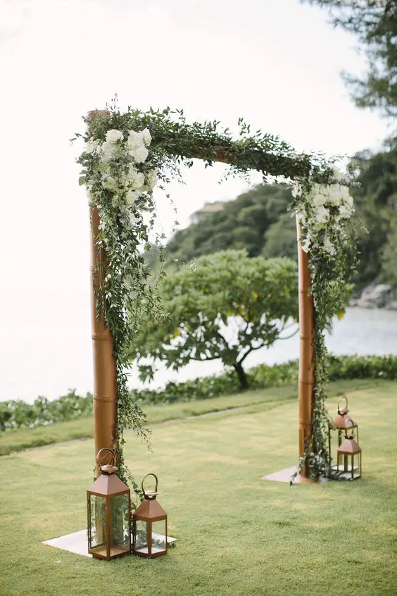 a traditional rustic wedding arch of brass pipes greenert and white hydrangeas plus vintage candle lanterns around