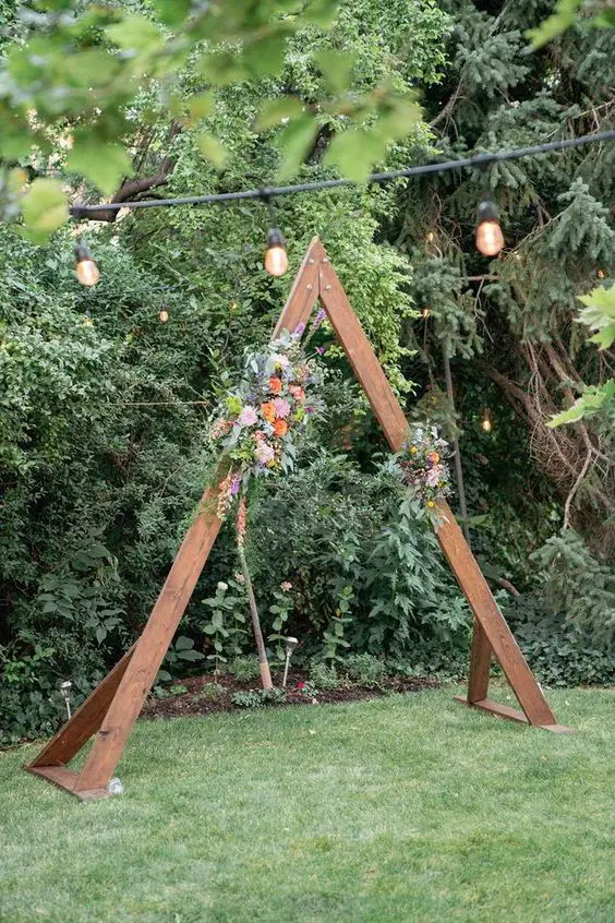 a very simple rustic wedding arch of rich stained wood bold blooms and greenery is a cool idea for a rustic or boho wedding