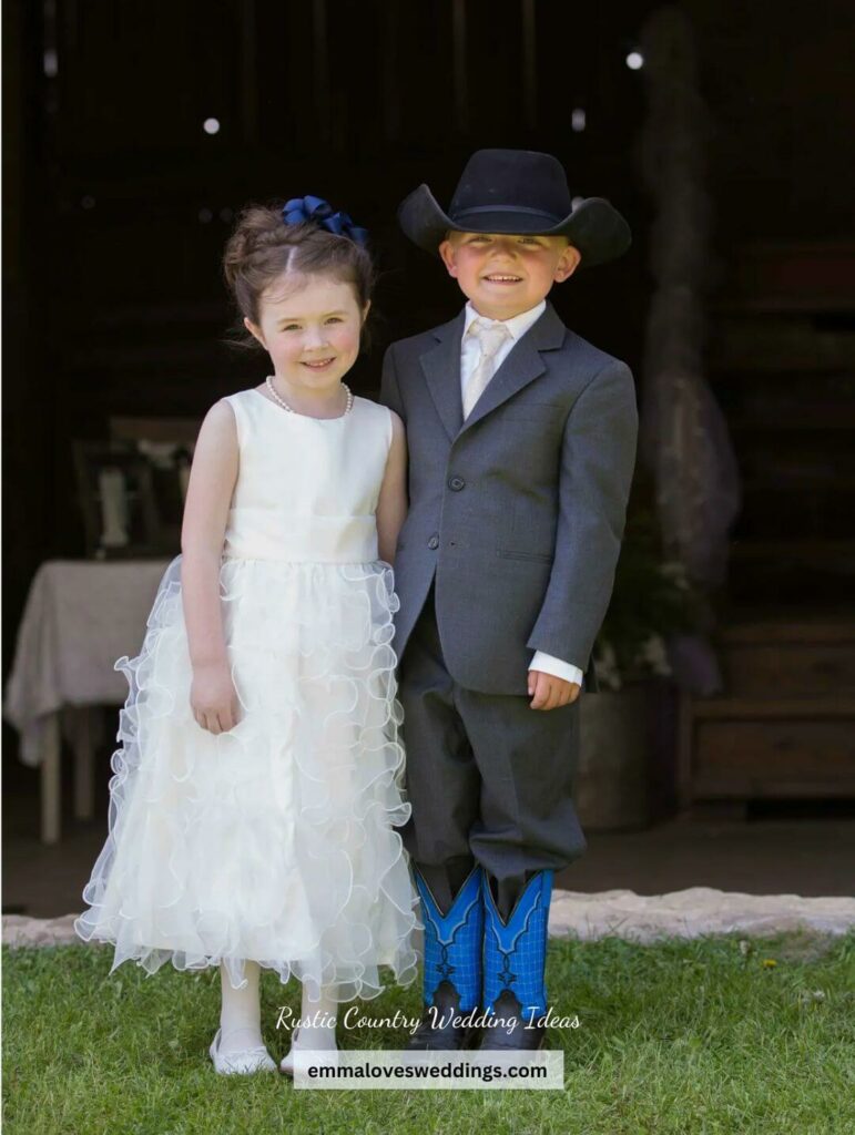Ring bearer looks handsome in a grey suit cowboy hat blue cowboy boots while the flower girl looks gorgeous in her white dress