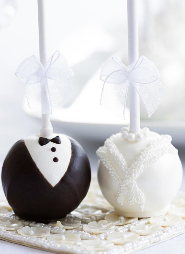 Beautiful cake pops in the guise of the bride and groom complete with tuxedos wedding gowns and white ribbon bows.