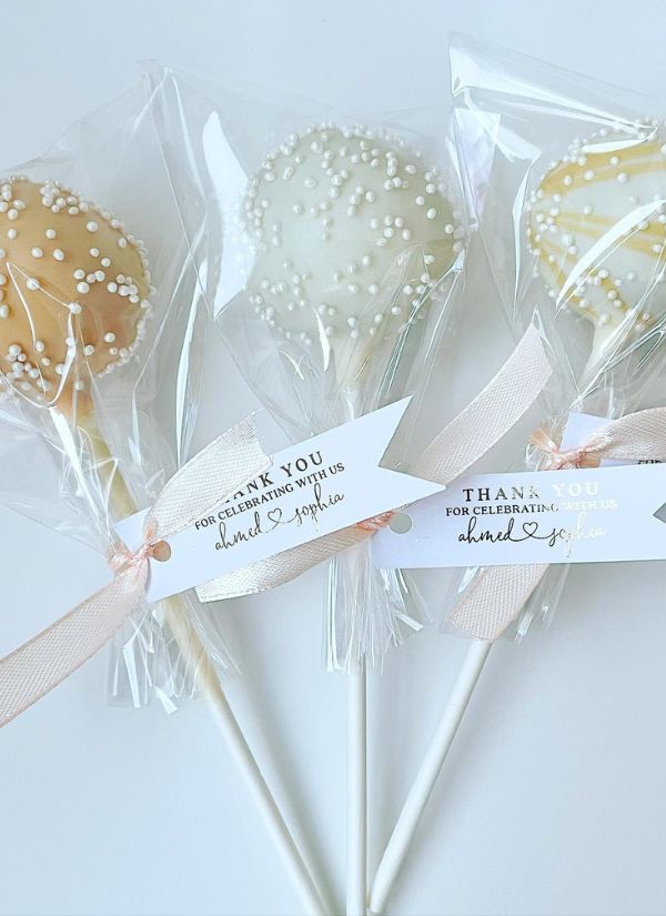 Beautiful wedding cake pop favors with a white and peach colour scheme each with a different flavor.
