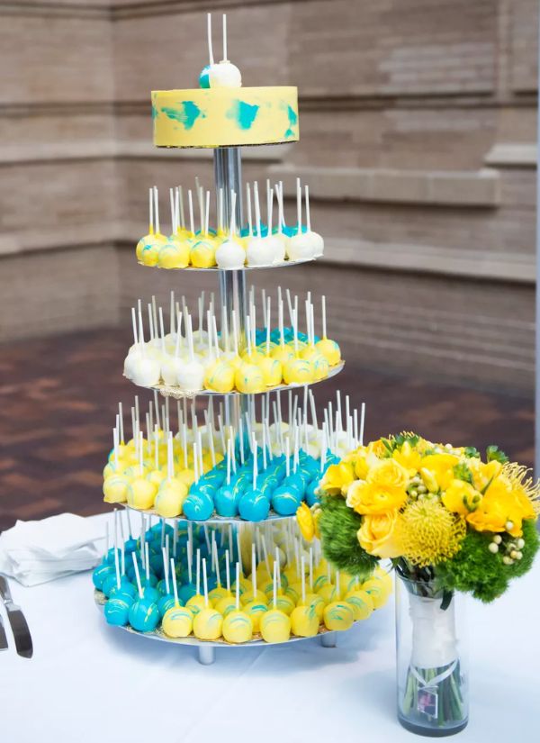 Cake pops in blue and yellow for a wedding with flavors like cheesecake, lemon, and chocolate peanut butter.