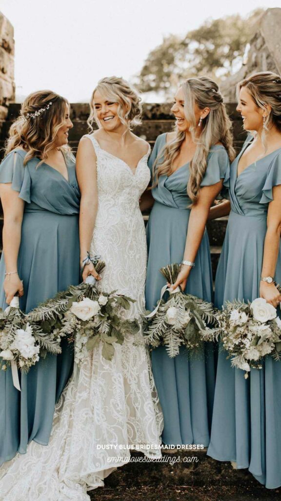 Cheerful bride in a white gown surrounded by bridesmaid dresses in dusty blue color