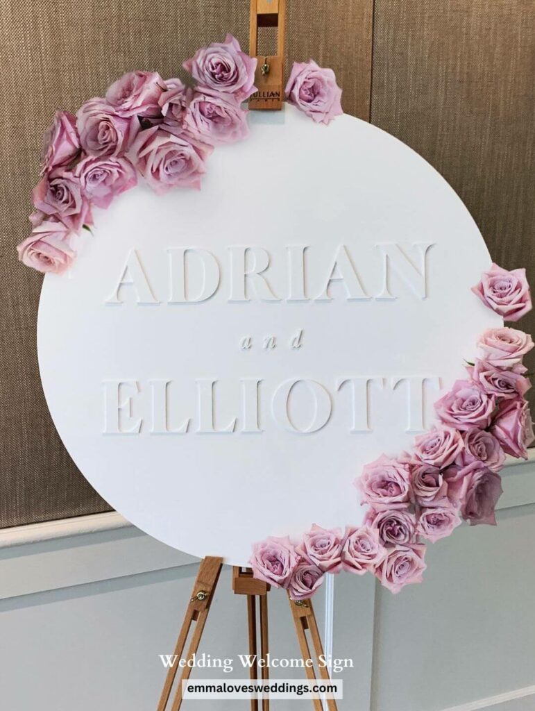 In breathtaking contrast to the white round wedding welcome sign, the pink flower stands out.