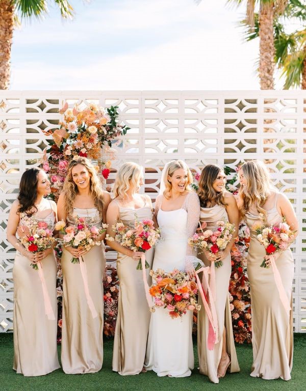 Satin dresses in a champagne color for the bridesmaids and a bouquet of bright flowers.
