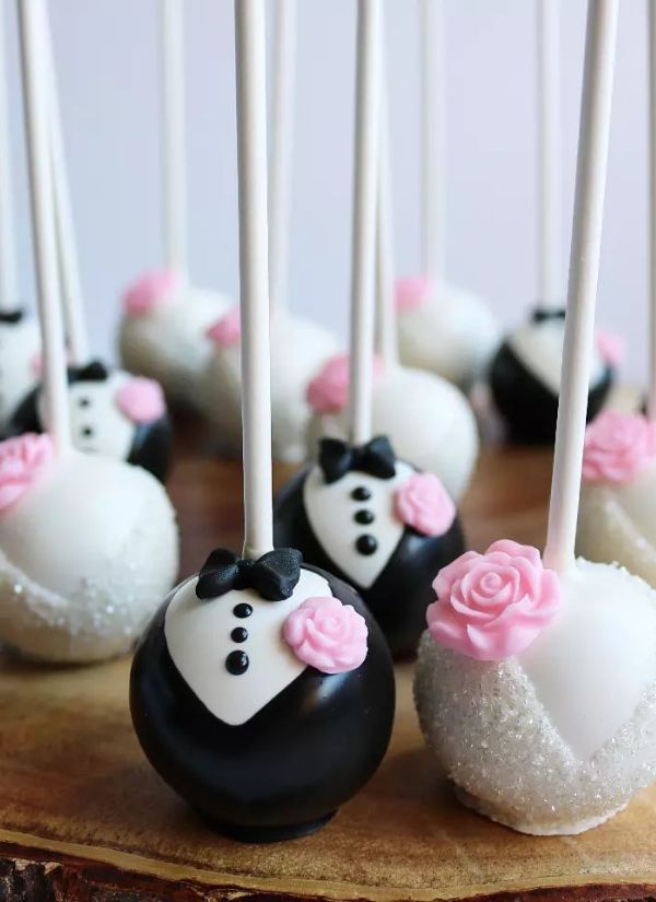 Taste and enjoy these bride and groom cake pops that are adorned with a pink flower.