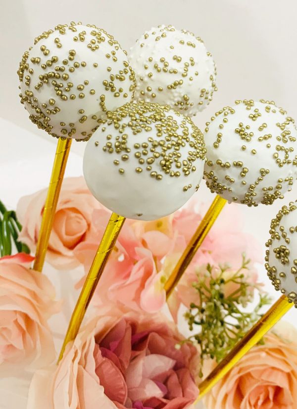 Wedding cake pops covered in white icing and sprinkled with gold ideal for any weddings theme.