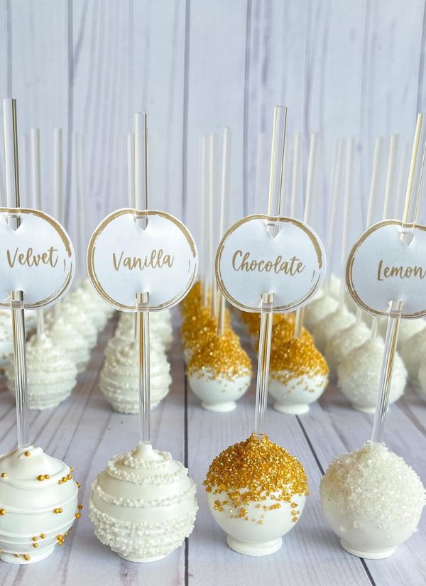 Wedding cake pops made of white wedding cake and adorned with gold can be served in a variety of flavors.