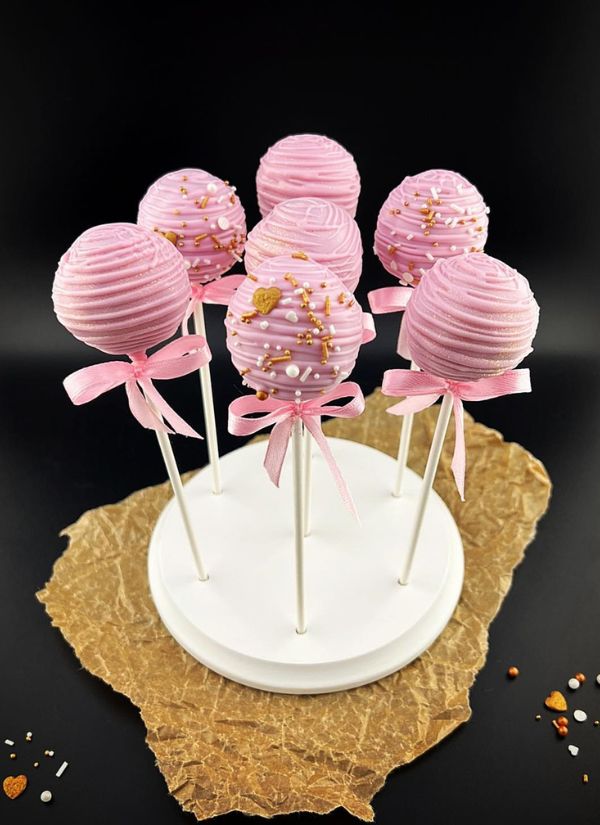 Wedding cake pops with a pink frosting gold sprinkles and a bow and ribbon for decoration.
