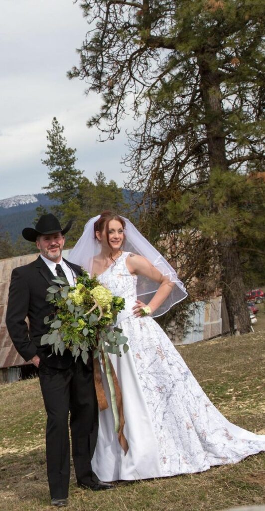 An elegant choice for a country or rustic wedding is a white Camo wedding dress with veil for the bride and a black tuxedo and hat for the groom.