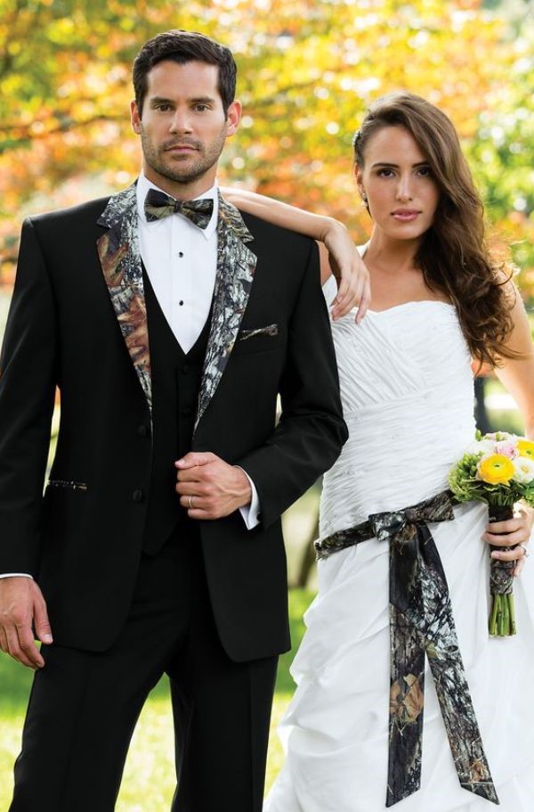 The bride in white with a camo waistline and bouquet and the groom in a camouflage patterned black tux make a striking couple.
