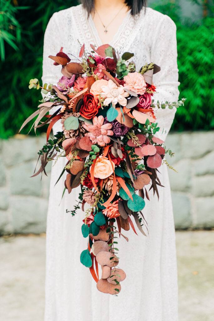 a beautiful fall wedding bouquet of blush, burgundy, orange blooms, greenery and dark foliage with much dimension is amazing