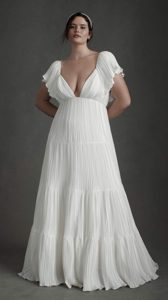 A plus size A line wedding dress with a plunging neckline and an empire waist from which luscious layers of pleated charmeuse cascade.
