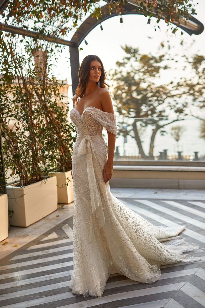 Ivory off the shoulder mermaid sexy lace wedding dress with sparkling golden fabric a heart shaped neckline front bow design open back and a delicate long train.