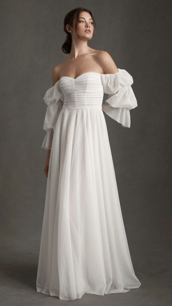 This corseted off the shoulder A-line wedding dress has exaggerated puff sleeves a modest train and layers of airy comfort.