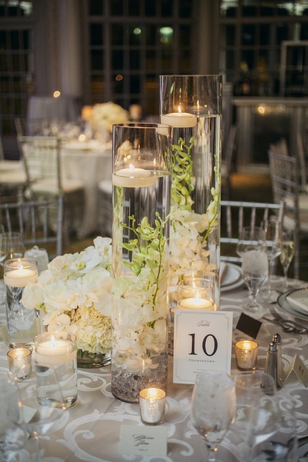 A breathtaking floating candle centerpiece with vivid flowers and flickering candles floating in a clear glass vase filled with water will enchant your wedding event.