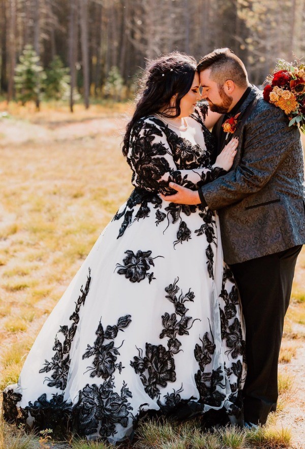 This plus size wedding dress is the epitome of beauty and grace it is a striking contrast of delicate black blossoms embellishing a white fabric.