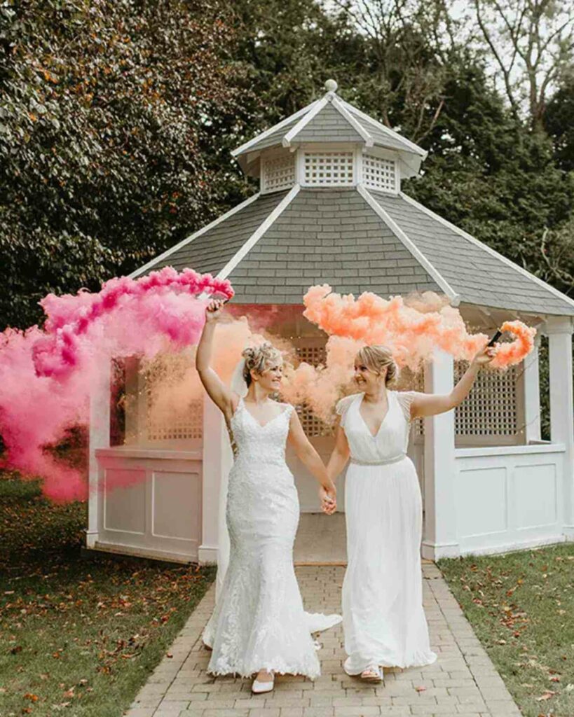 lesbian brides in gorgeous wedding gown holding pink and orange smoke bomb