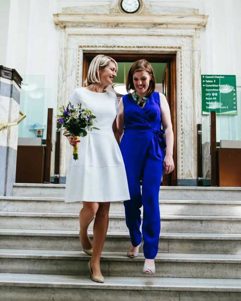 two brides in white short dress and cobalt blue jumpsuit for lesbian wedding