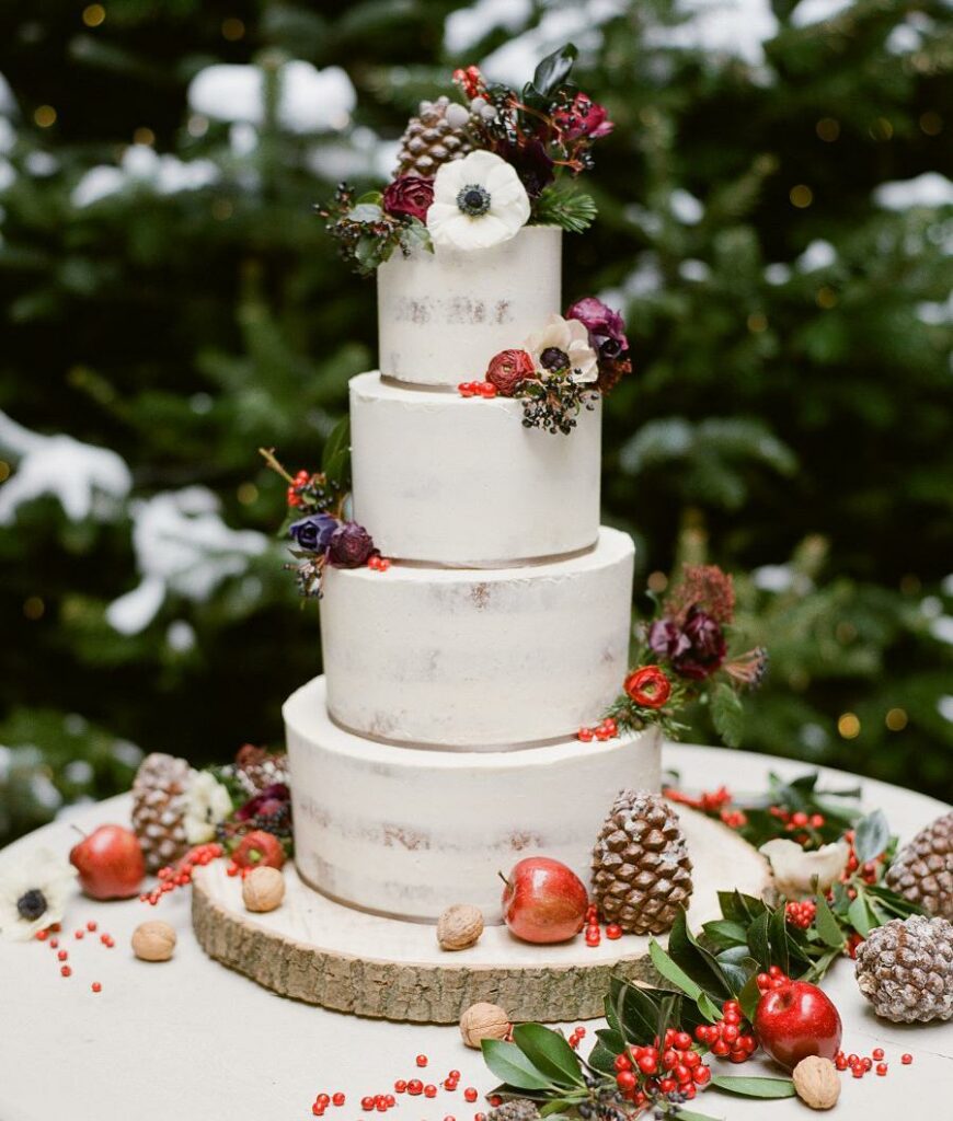four tiered winter Christmas wedding cake with pinecones fresh flowers and greenery