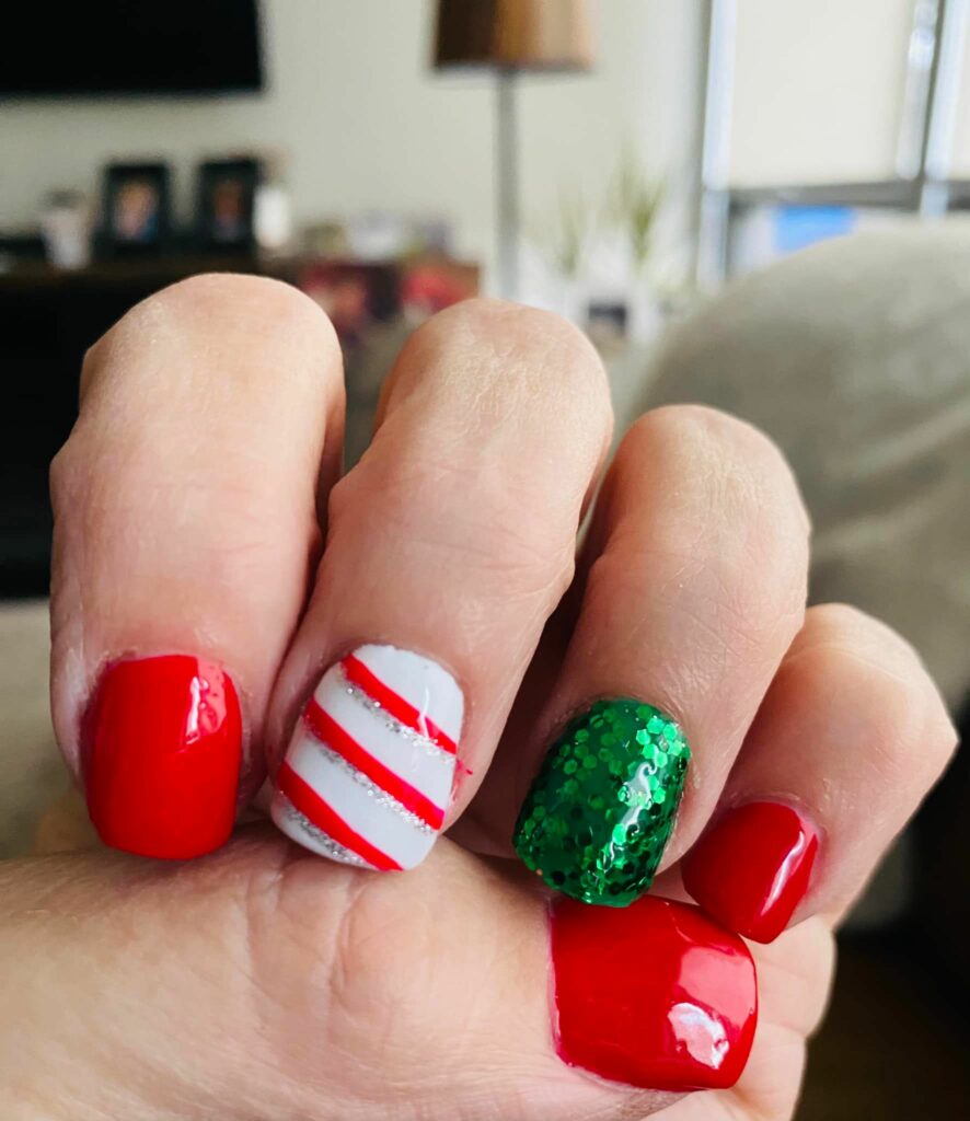 glossy reds Christmas nails with a festive candy cane accent and a touch of green glitter