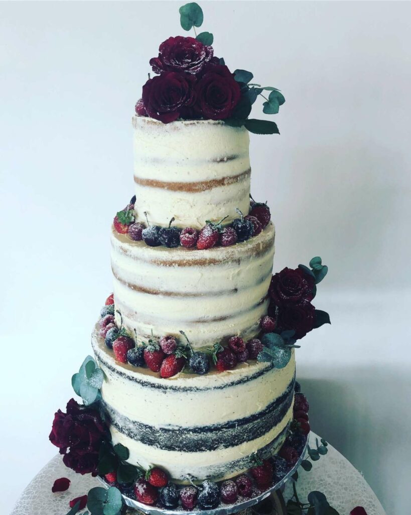 naked wedding cake design with winter frosted berries and deep roses