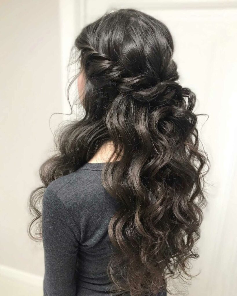 A half up hairstyle with lustrous black hair waves and a delicate twist is charming