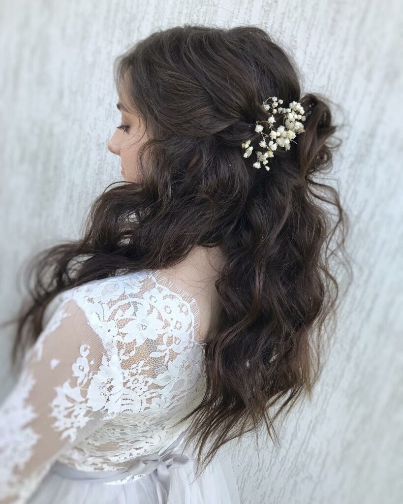 Soft cascading curls adorned with delicate white florals create a romantic, bohemian half up hairstyle on raven black locks