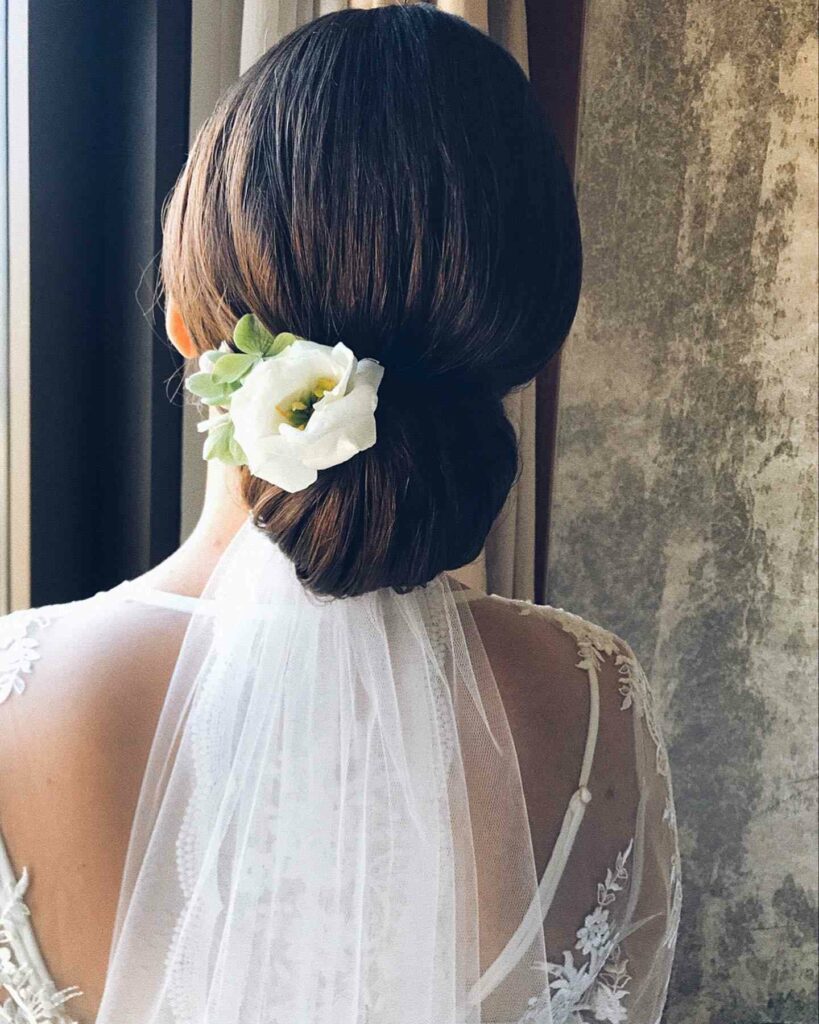 simple and chic low bun bridal hairstyle with flower and veil