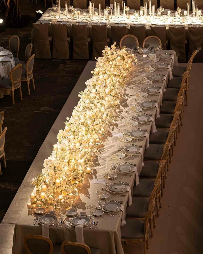 wedding reception setup with an overflowing centerpiece of white orchids and votive candles